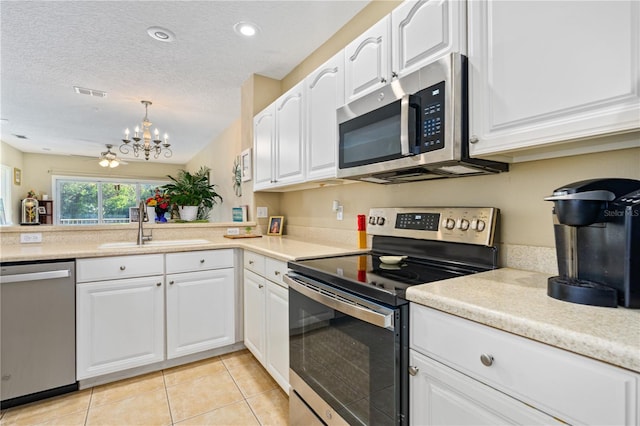 kitchen with appliances with stainless steel finishes, ceiling fan with notable chandelier, sink, pendant lighting, and white cabinetry