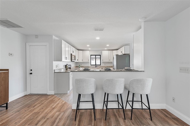 kitchen with white cabinetry, kitchen peninsula, wood-type flooring, a kitchen bar, and appliances with stainless steel finishes