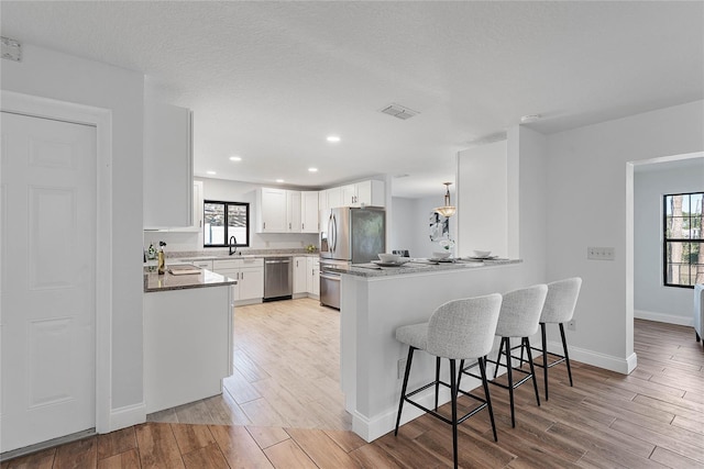 kitchen featuring kitchen peninsula, a textured ceiling, a breakfast bar area, white cabinets, and appliances with stainless steel finishes