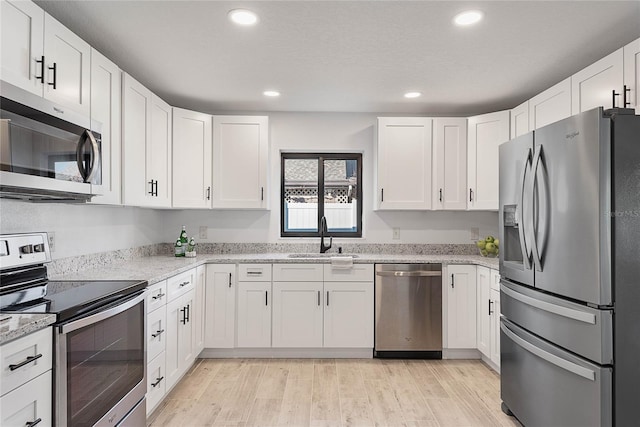 kitchen featuring white cabinets, sink, light wood-type flooring, light stone counters, and stainless steel appliances