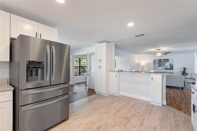 kitchen with white cabinets, stainless steel fridge, light stone counters, and light hardwood / wood-style floors