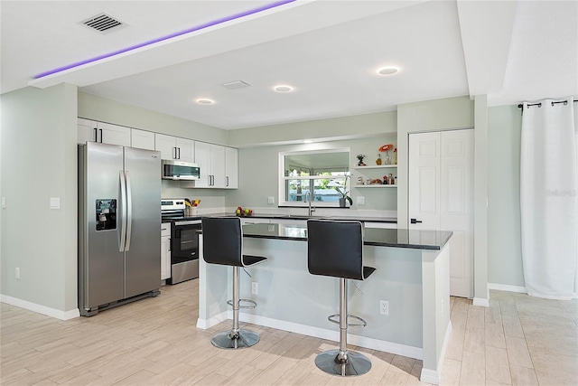 kitchen featuring a center island, a breakfast bar area, light wood-type flooring, white cabinetry, and stainless steel appliances