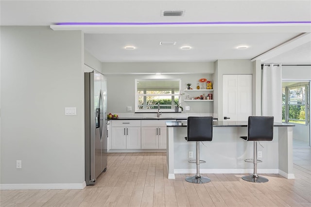 kitchen featuring white cabinets, sink, stainless steel fridge, a healthy amount of sunlight, and a breakfast bar area