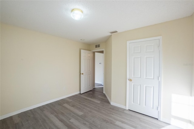 unfurnished bedroom with a textured ceiling, light hardwood / wood-style floors, and a closet