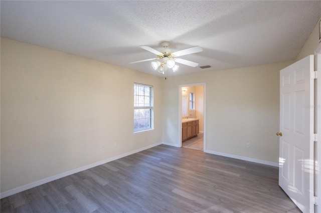 unfurnished bedroom with a textured ceiling, ceiling fan, dark wood-type flooring, and connected bathroom