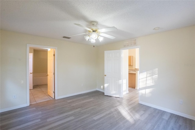 unfurnished bedroom featuring a textured ceiling, hardwood / wood-style flooring, ensuite bath, and ceiling fan