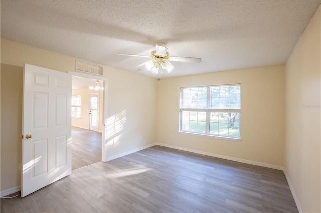 empty room with hardwood / wood-style flooring, ceiling fan with notable chandelier, and a textured ceiling