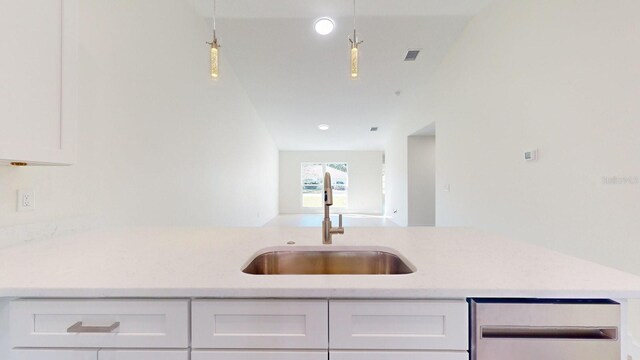 kitchen featuring light stone countertops, white cabinetry, sink, and hanging light fixtures