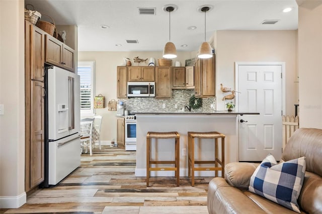 kitchen featuring tasteful backsplash, light hardwood / wood-style flooring, decorative light fixtures, white appliances, and a breakfast bar