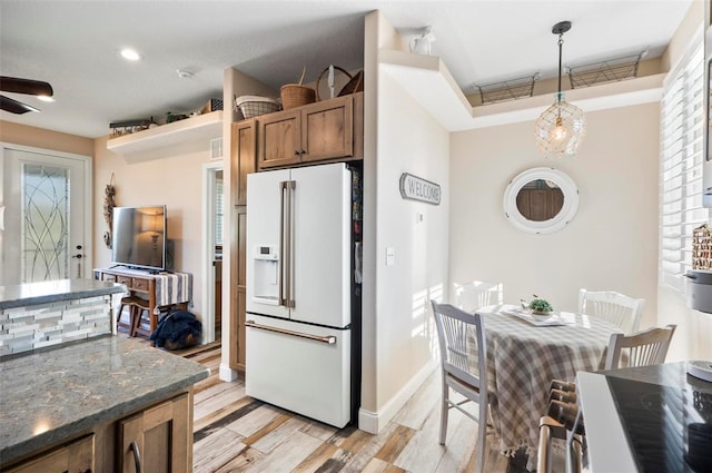 kitchen with dark stone counters, high end white refrigerator, pendant lighting, and light wood-type flooring