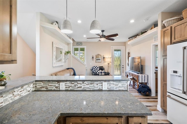 kitchen featuring light wood-type flooring, ceiling fan, decorative light fixtures, dark stone countertops, and white fridge with ice dispenser