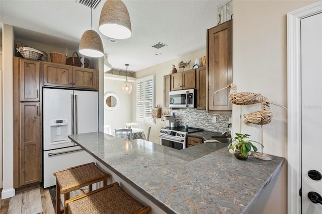 kitchen with light hardwood / wood-style flooring, kitchen peninsula, pendant lighting, decorative backsplash, and appliances with stainless steel finishes