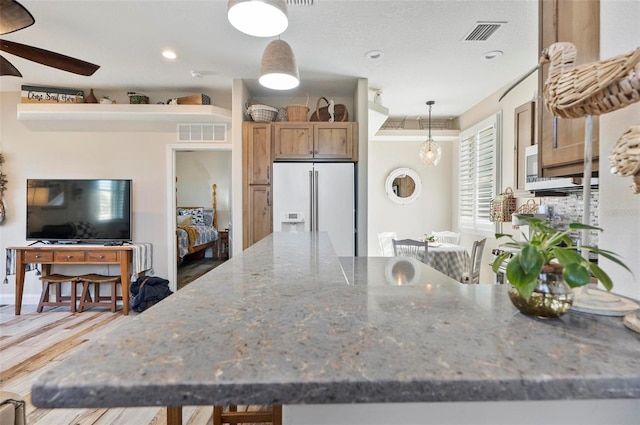 kitchen featuring stone countertops, hardwood / wood-style flooring, ceiling fan, white fridge with ice dispenser, and decorative light fixtures