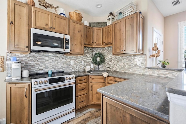 kitchen featuring backsplash, dark stone counters, white electric stove, light hardwood / wood-style flooring, and kitchen peninsula