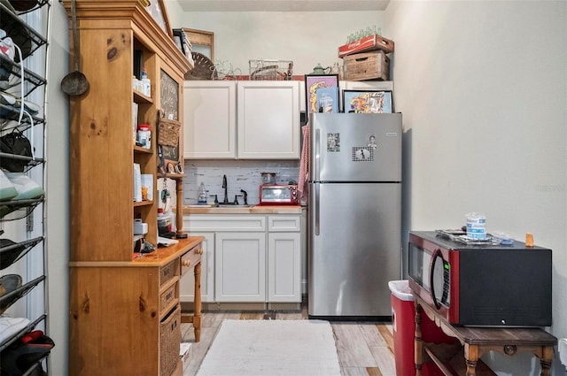 kitchen featuring stainless steel fridge, light wood-type flooring, tasteful backsplash, sink, and white cabinets