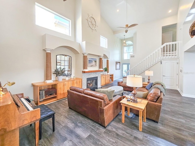 living room with decorative columns, ceiling fan, dark wood-type flooring, and a high ceiling