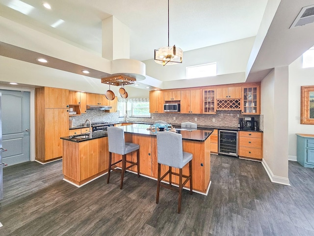 kitchen with a towering ceiling, a kitchen island, dark wood-type flooring, pendant lighting, and wine cooler