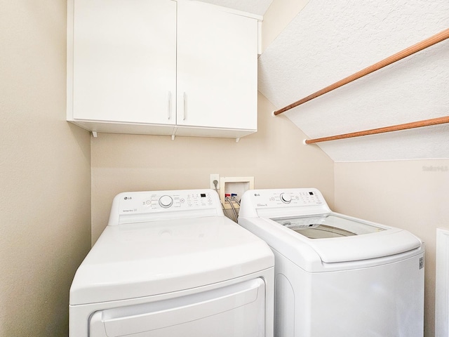 clothes washing area with washing machine and clothes dryer and cabinets