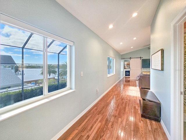 corridor with plenty of natural light, a barn door, a water view, and lofted ceiling