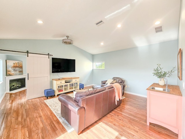 living room featuring a barn door, light wood-type flooring, lofted ceiling, and sink