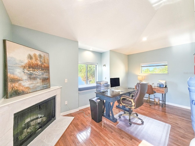 home office featuring a tile fireplace and light hardwood / wood-style flooring