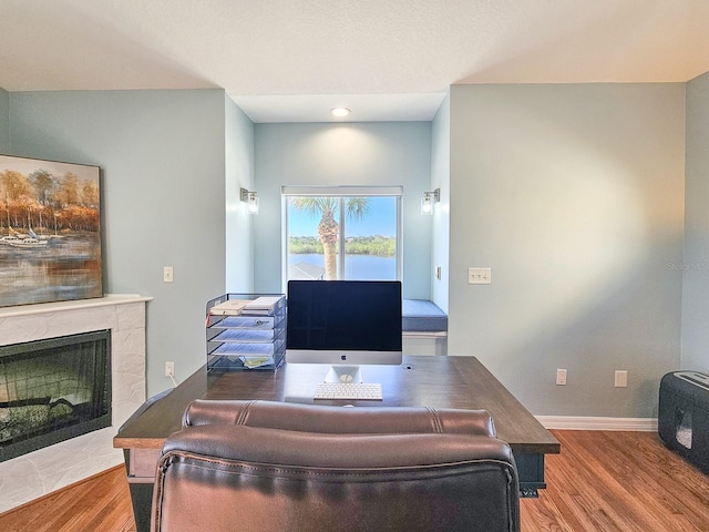 home office featuring a tiled fireplace and hardwood / wood-style floors