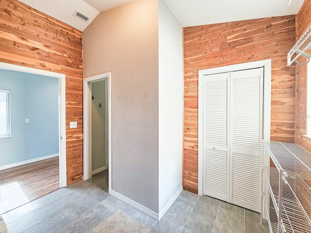 unfurnished bedroom featuring tile patterned flooring, vaulted ceiling, a closet, and wooden walls