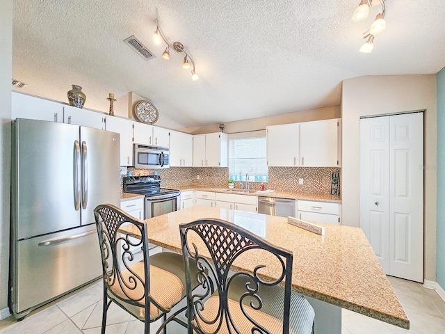 kitchen with stainless steel appliances, white cabinetry, a center island, and lofted ceiling