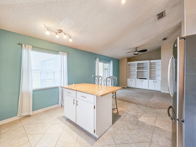 kitchen featuring vaulted ceiling, a breakfast bar, a kitchen island, white cabinetry, and stainless steel refrigerator