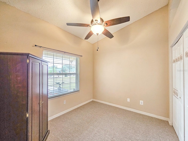 unfurnished bedroom featuring lofted ceiling, a textured ceiling, ceiling fan, and light colored carpet