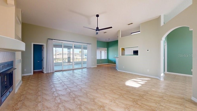 unfurnished living room with ceiling fan, a fireplace, and a high ceiling