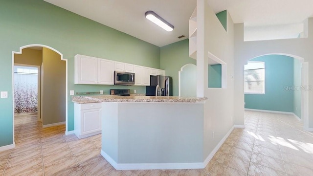 kitchen with white cabinetry, stainless steel appliances, light stone counters, a towering ceiling, and light tile patterned floors