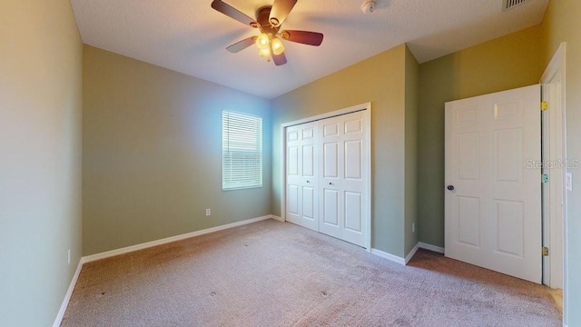 unfurnished bedroom featuring light carpet, a textured ceiling, a closet, and ceiling fan