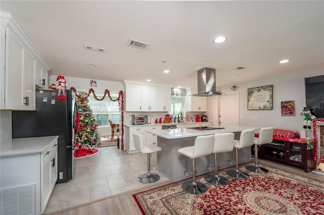 kitchen with sink, white cabinetry, a kitchen breakfast bar, a center island, and island exhaust hood