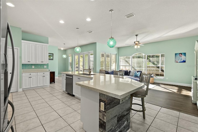 kitchen with tasteful backsplash, ceiling fan, light tile patterned floors, white cabinetry, and an island with sink