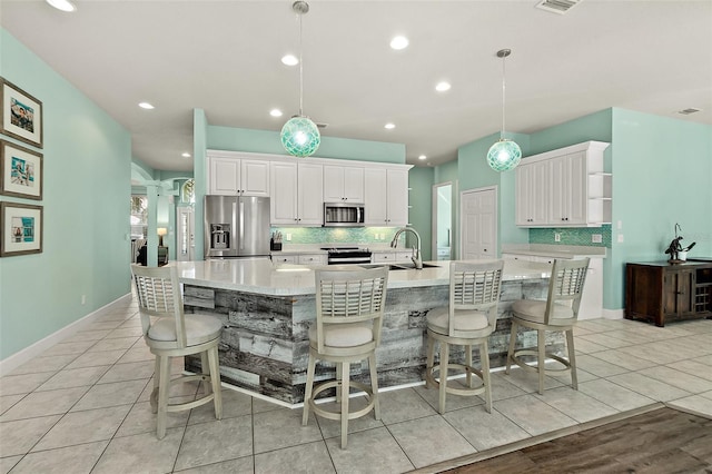 kitchen with white cabinets, a spacious island, decorative light fixtures, light tile patterned floors, and appliances with stainless steel finishes