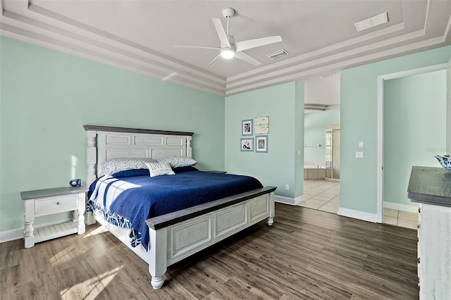 bedroom featuring dark hardwood / wood-style flooring, ensuite bath, a raised ceiling, and ceiling fan