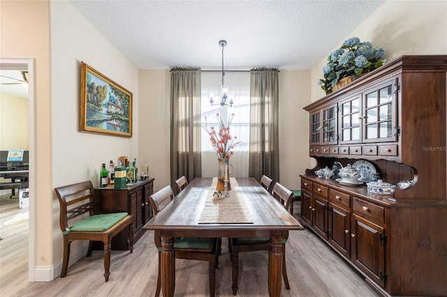 dining room with a notable chandelier, light wood-type flooring, and a textured ceiling