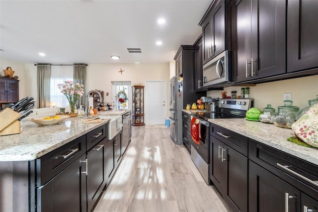 kitchen with sink, stainless steel appliances, light hardwood / wood-style flooring, and light stone counters