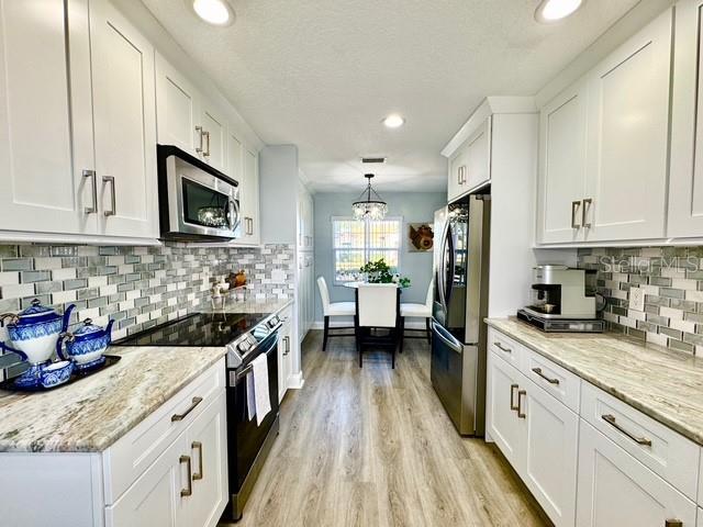 kitchen featuring light stone countertops, white cabinetry, light hardwood / wood-style floors, pendant lighting, and appliances with stainless steel finishes