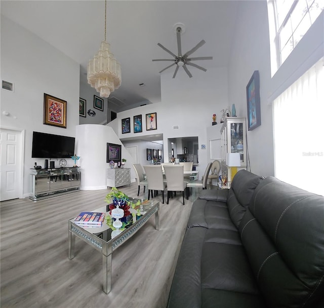 living room with ceiling fan with notable chandelier, wood-type flooring, and a towering ceiling