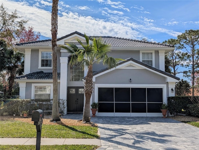 traditional home featuring a garage, a tile roof, decorative driveway, and stucco siding