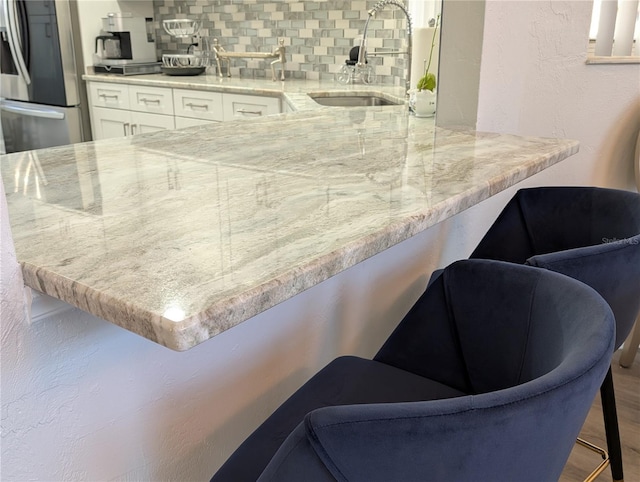 kitchen featuring a breakfast bar area, a sink, white cabinetry, stainless steel refrigerator with ice dispenser, and decorative backsplash