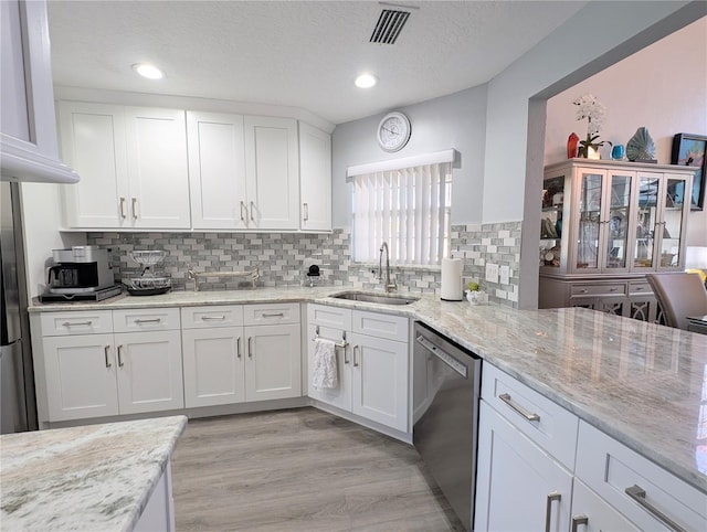 kitchen featuring a sink, white cabinetry, light wood-style floors, light stone countertops, and dishwasher