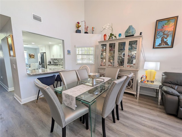 dining area featuring a towering ceiling, light wood-style flooring, visible vents, and baseboards