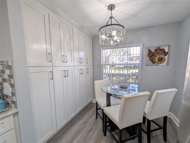 dining room featuring light wood-style floors, a chandelier, a textured ceiling, and baseboards