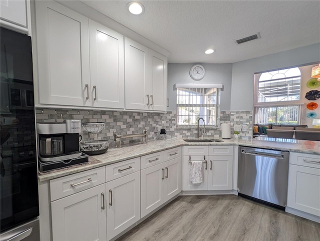 kitchen with visible vents, light wood-style flooring, stainless steel dishwasher, white cabinetry, and a sink