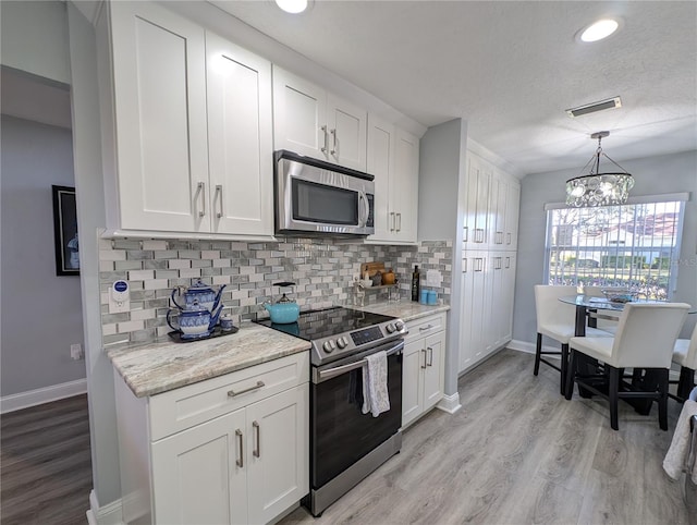 kitchen with light wood-style flooring, stainless steel appliances, visible vents, white cabinets, and tasteful backsplash