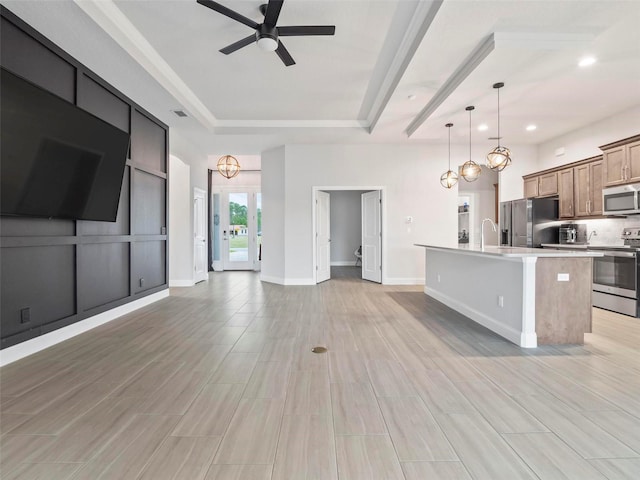 kitchen featuring ceiling fan, light countertops, appliances with stainless steel finishes, a raised ceiling, and open floor plan