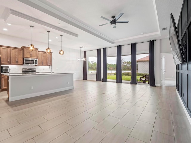 kitchen with ceiling fan, open floor plan, brown cabinetry, stainless steel appliances, and a raised ceiling